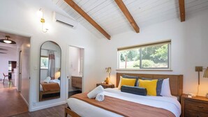 A bedroom with a large bed, wooden beams, a window, and a mirror.