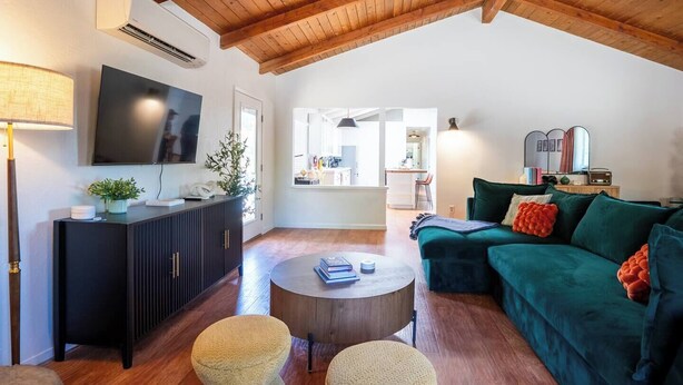 A spacious living area with a high ceiling, a flat-screen TV, a dark wooden cabinet, a green sofa, and a round coffee table.