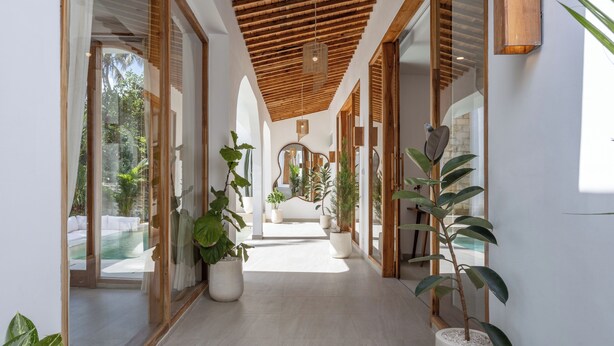 A modern hallway with wooden ceiling beams, large windows, and potted plants. - Luxurious 2BR Villa - Scenic Rice Field Views - Beautiful Swimming Pool & Garden (Canggu)