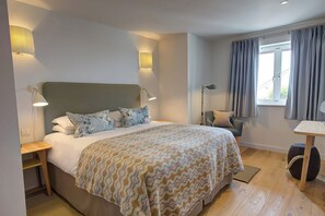 Um quarto moderno com uma cama grande, duas luminárias de cabeceira, uma cadeira, uma mesinha e uma janela com cortinas.