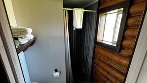 A compact bathroom with a toilet, a small shelf with towels, a window, and a wooden wall.