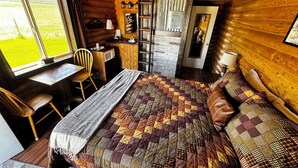 A cozy log cabin room with a large bed, a desk, and a chair.