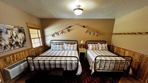 Une chambre avec deux lits, un ventilateur de plafond, une fenêtre avec des stores, un radiateur et un grand tableau au mur.