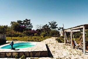A stone-paved outdoor area with a swimming pool, a hammock, and a pergola.