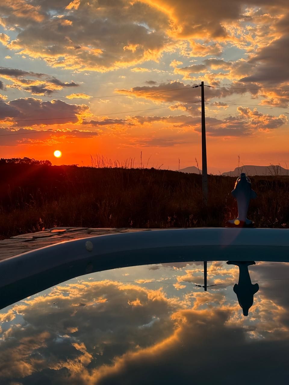 A sunset with clouds reflected in a body of water, a utility pole, and a fire hydrant.