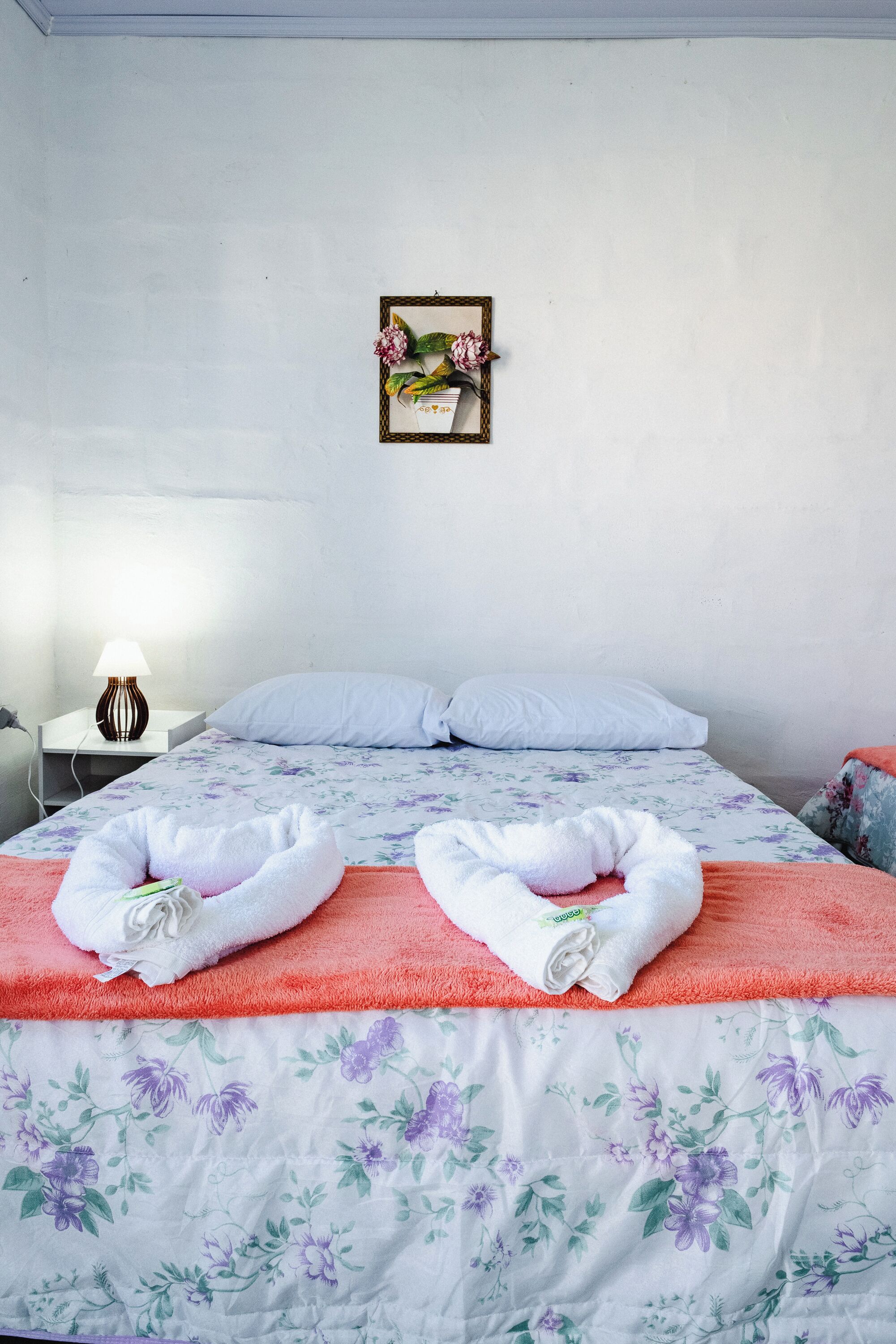 A neatly made bed with floral bedding, a white pillow, and two towels on the bed.