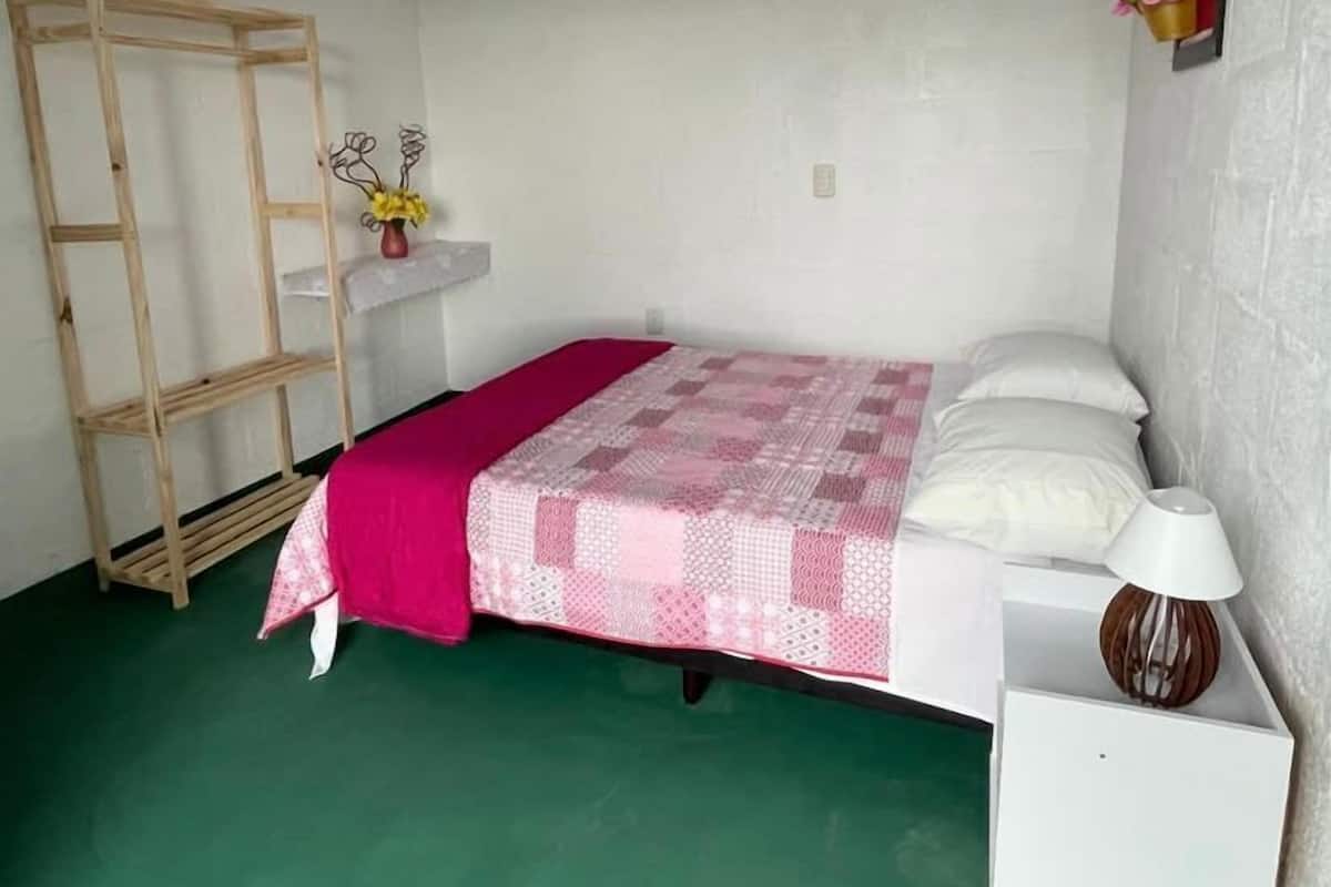 A small, single-bed room with a wooden ladder, a bedside table with a lamp, and a wall-mounted shelf with flowers.