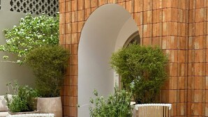 Un espacio de estar al aire libre con mobiliario de mimbre, una jardinera central y un muro de ladrillo.
