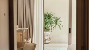 Habitación de hotel moderna con una cama grande, una silla de madera, una mesita pequeña y una planta en maceta.