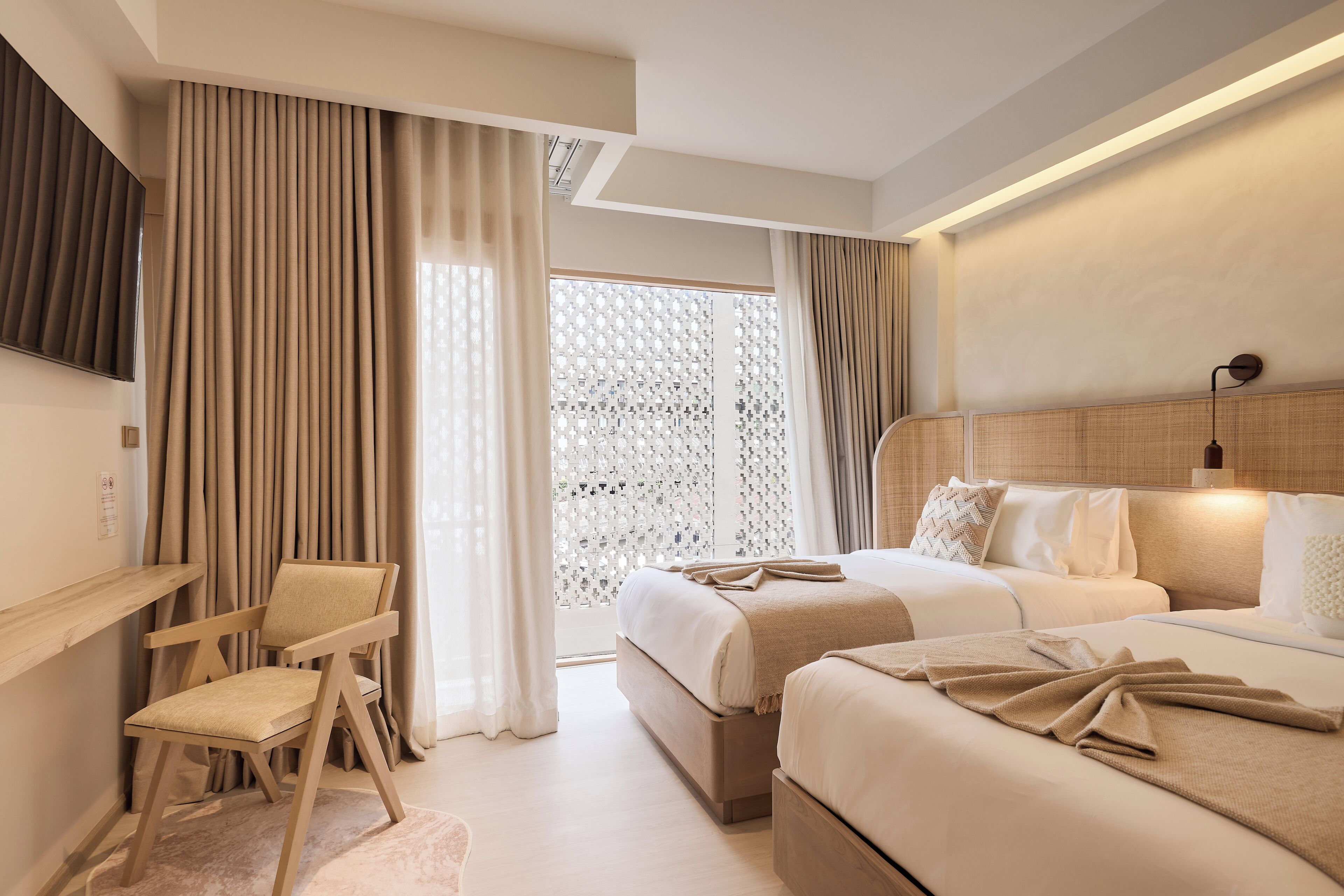 A modern hotel room with two beds, a desk, and a large window with curtains.