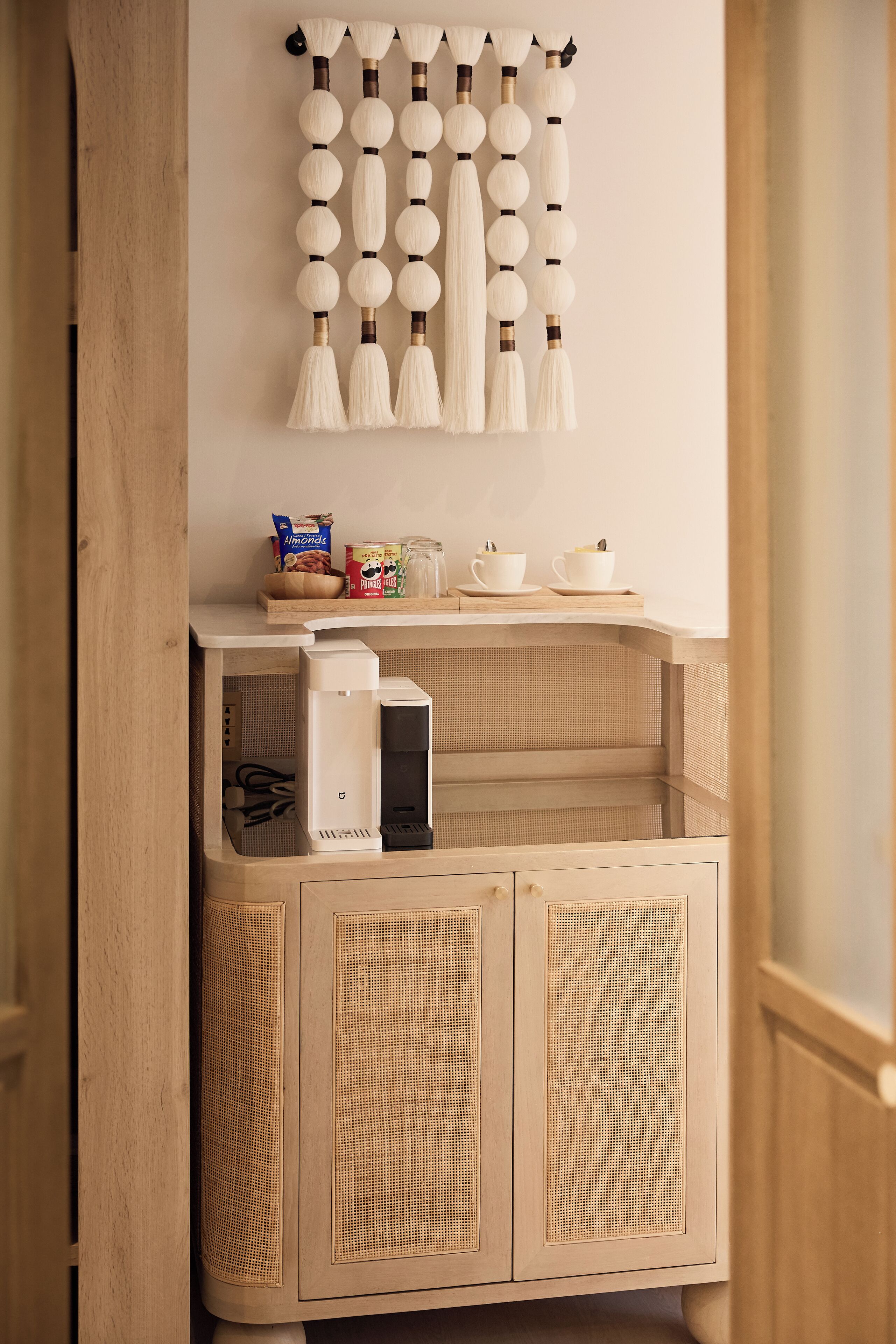 A kitchen area with a wooden cabinet, a coffee machine, and a hanging light fixture.