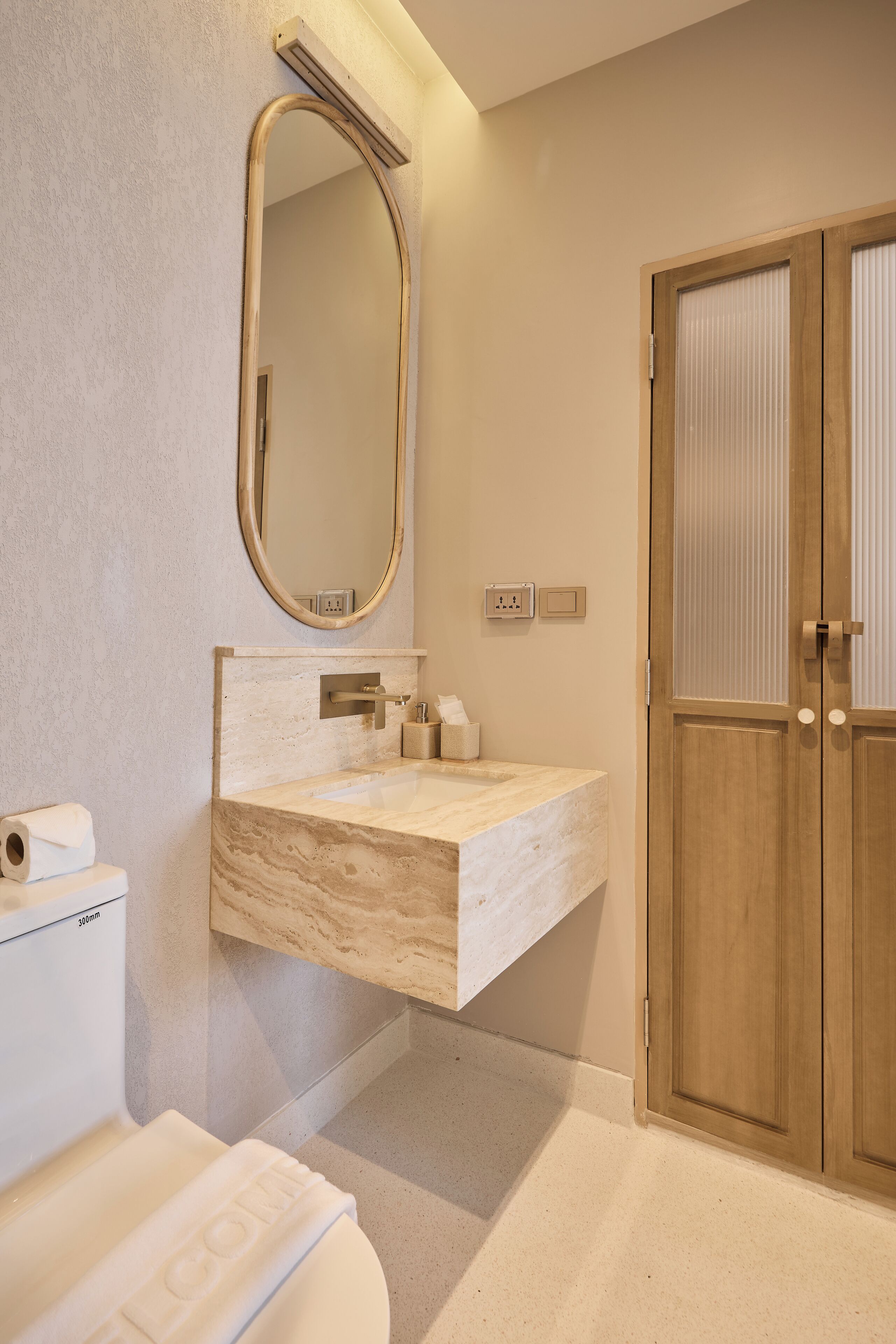 A bathroom with a marble sink, a toilet, a mirror, and a wooden door.