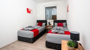 A modern bedroom with two beds, a small bedside table with a lamp, and a window with a view. - Livemore24 - Apartment 3 in Duisburg 24/7 check-in (Duisburg)