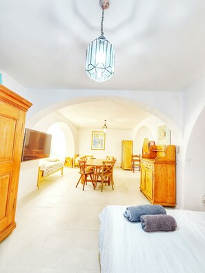 Ein geräumiges Zimmer mit einem Bett, einem Esstisch, Stühlen, Holzschränken und einem Fernseher.