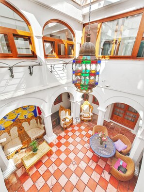 Ein mehrgeschossiges Interieur mit einem Schachbrettmuster-Boden, verzierten Stühlen, einem hängenden Laternen und einer Wand mit Muster.