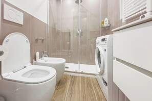 Modern bathroom with a glass-enclosed shower, handheld showerhead, and washing machine.