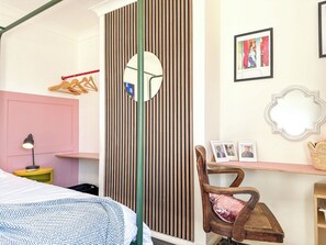 Un dormitorio con una cama, una mesita de noche con lámpara, una silla, un espejo y una pared con listones de madera verticales.