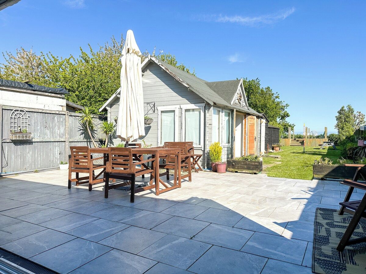 A patio with a table and chairs, a covered umbrella, and a garden area with a wooden fence.