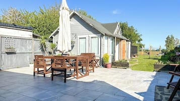 A patio with a table and chairs, a covered umbrella, and a garden area with a wooden fence.
