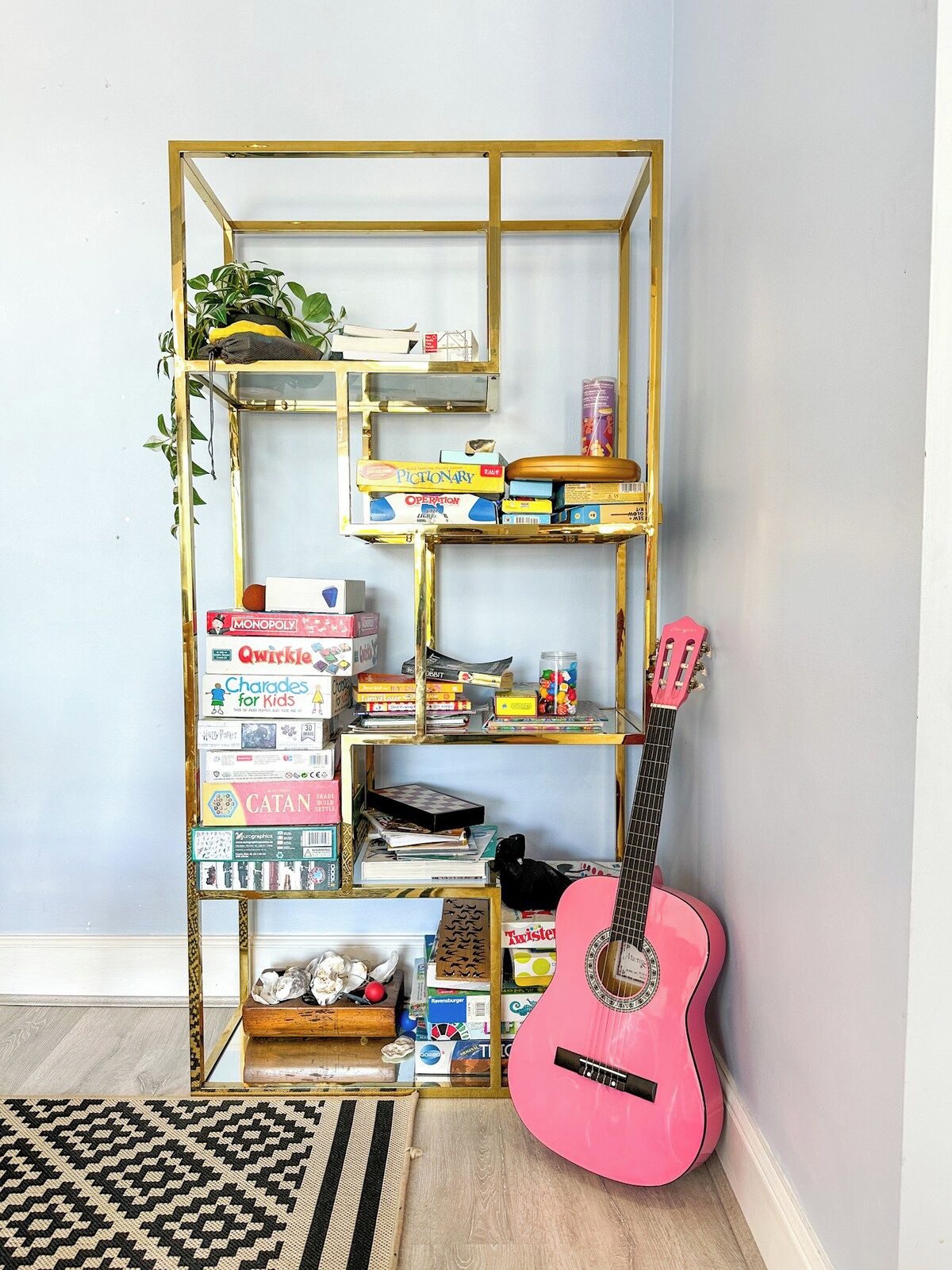 Une bibliothèque remplie de divers jeux de société et une guitare rose adossée à un mur.