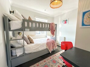Un lit superposé avec un bureau et une chaise, un tapis à motifs et une fenêtre avec des stores.