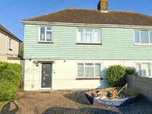 Une maison à deux étages avec une porte d’entrée, des fenêtres et un petit jardin agrémenté d’un bateau.