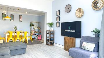 A modern living room with a sofa, a television, and a dining area with yellow chairs.