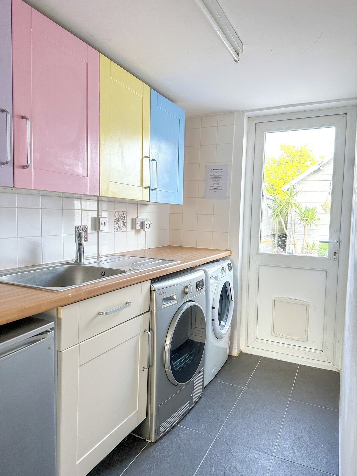 A compact kitchen with a washing machine, a sink, and cabinets in pastel colors.