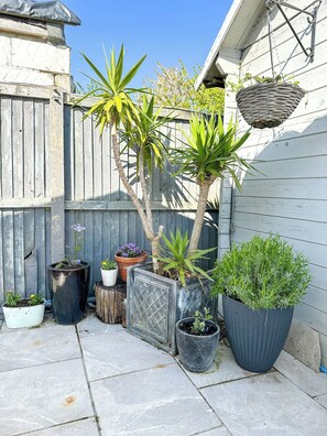 Un petit espace extérieur agrémenté de différentes plantes en pot, d’une jardinière suspendue et d’une clôture en bois.