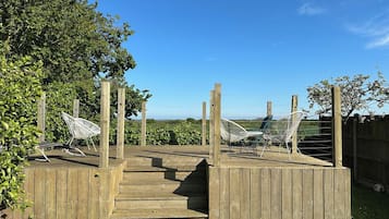 A wooden deck with a ramp leading to a raised platform, surrounded by a wooden fence and greenery.