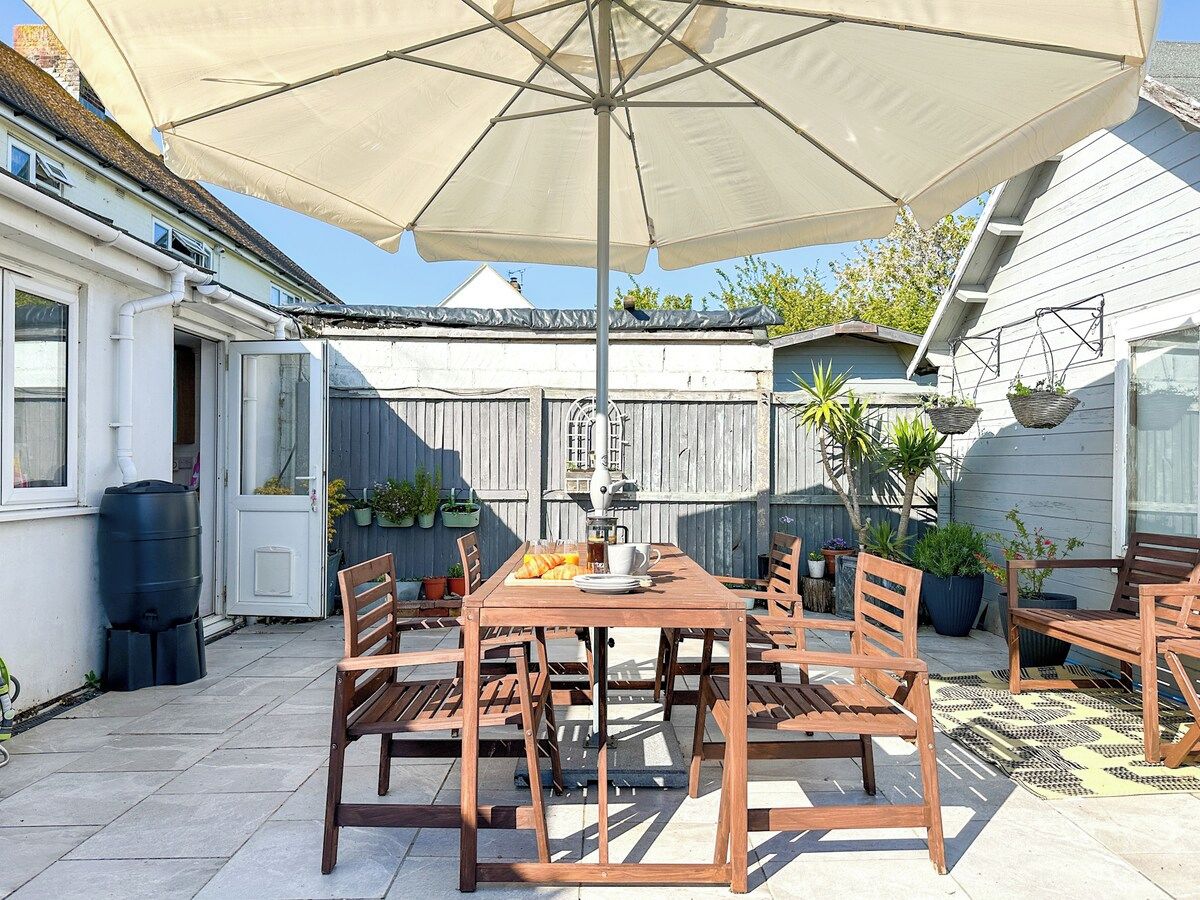 Eine Terrasse im Freien mit Holztisch und -stühlen, einem großen Sonnenschirm und Pflanzkübeln.