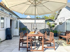 An outdoor patio with a wooden table and chairs, a large umbrella, and potted plants.