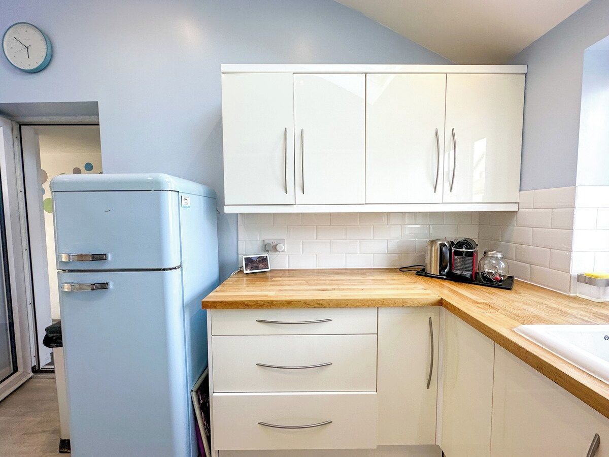 Eine Küche mit weißen Schränken, einem blauen Kühlschrank, einer Holz Arbeitsplatte und einer Uhr an der Wand.
