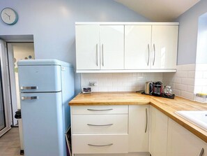A kitchen with white cabinets, a blue refrigerator, a wooden countertop, and a clock on the wall.