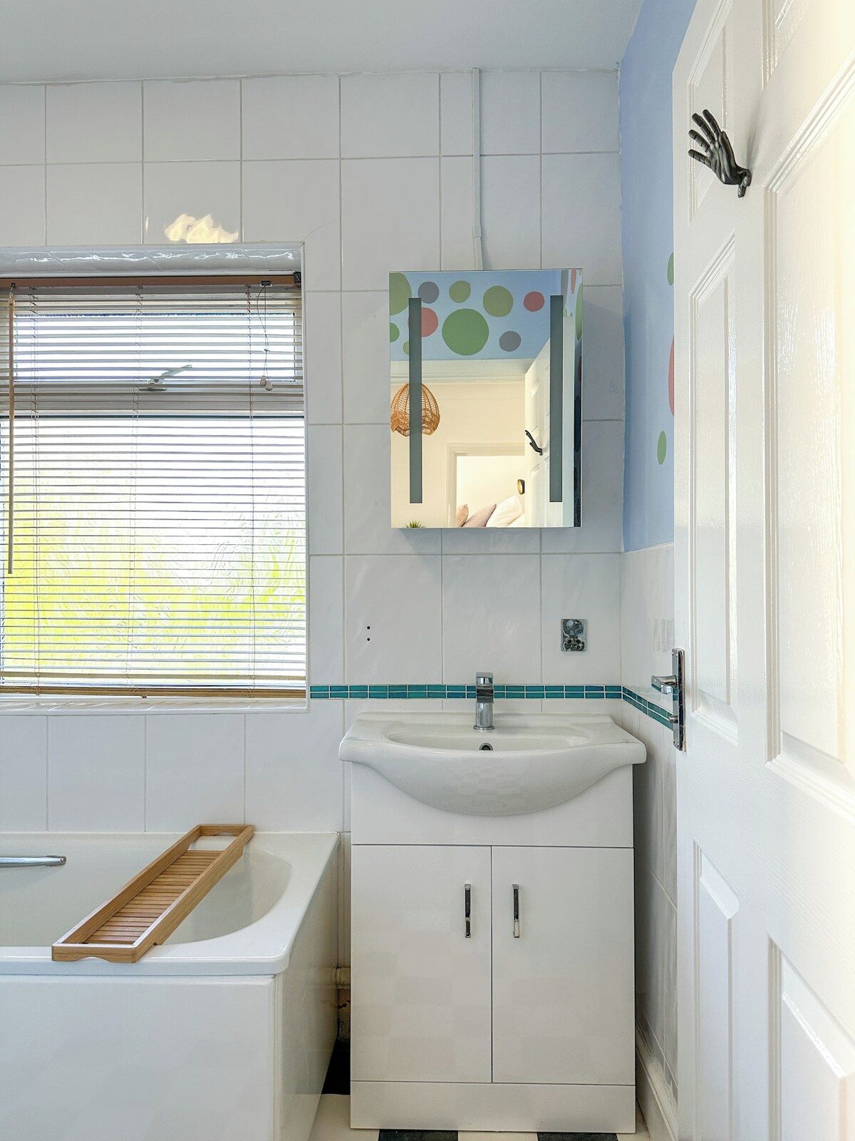 Un bagno con un lavandino bianco, uno specchio decorato con pois e una finestra con persiane.