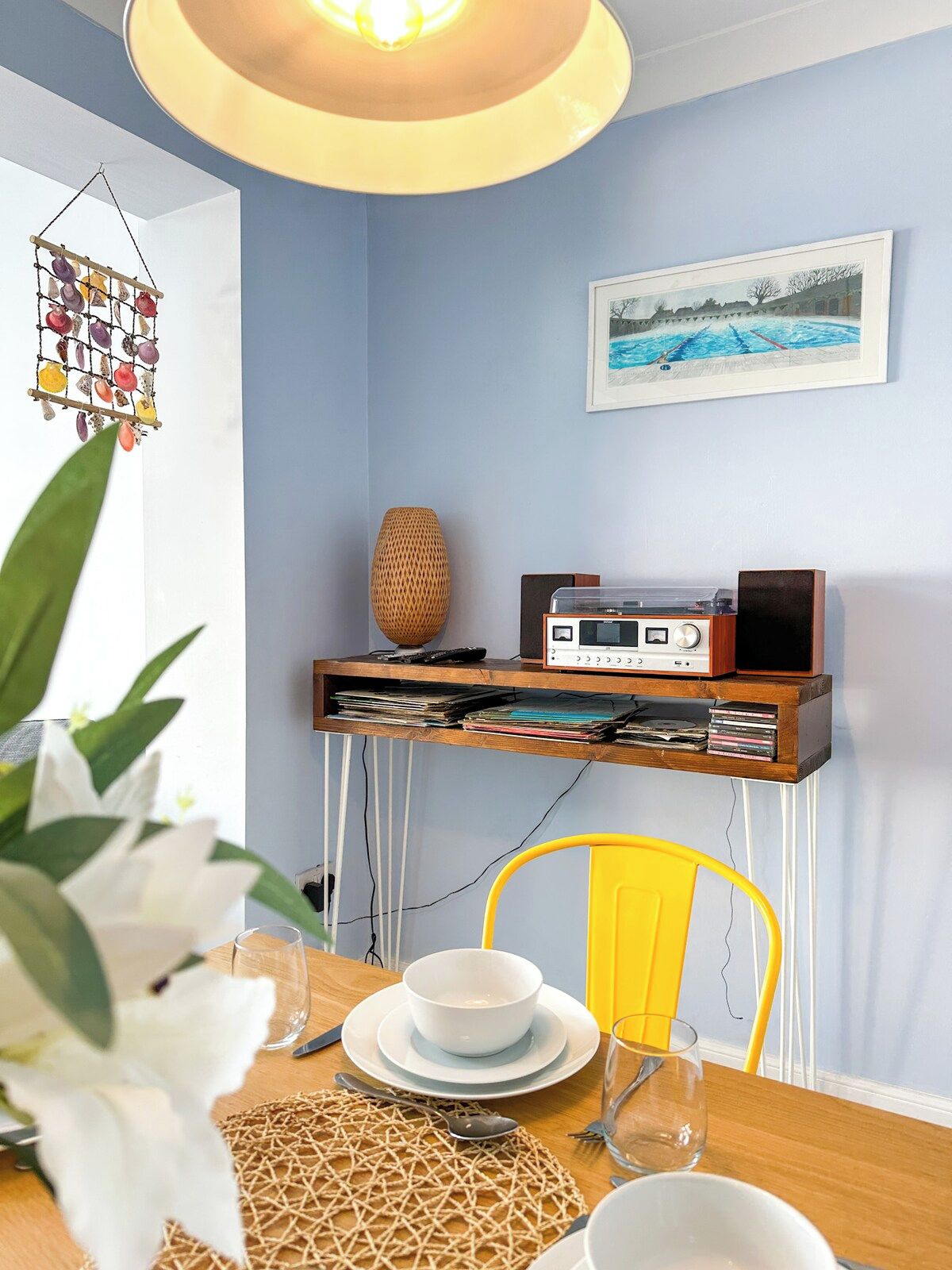 A dining area with a table set for two, a radio on a shelf, a framed picture on the wall, and a hanging decoration.