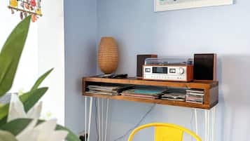 A dining area with a table set for two, a radio on a shelf, a framed picture on the wall, and a hanging decoration.