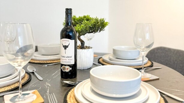 Una mesa de comedor dispuesta con platos blancos, una botella de vino y una pequeña planta en maceta.