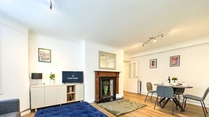 Una sala de estar moderna con un sofá azul, una chimenea, un comedor con sillas, un televisor y un aparador.