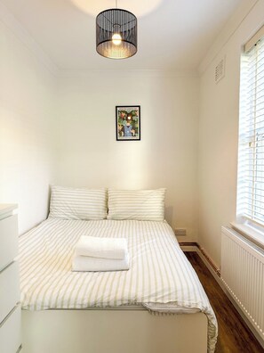 Ein Schlafzimmer mit einem Bett, einer Hängelampe, einem gerahmten Bild an der Wand und einem Fenster mit Jalousien.