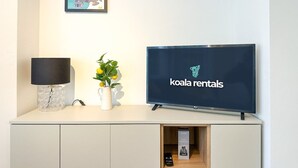 Una habitación moderna con una televisión mostrando 'koala rentals', una lámpara y un cuadro en la pared.