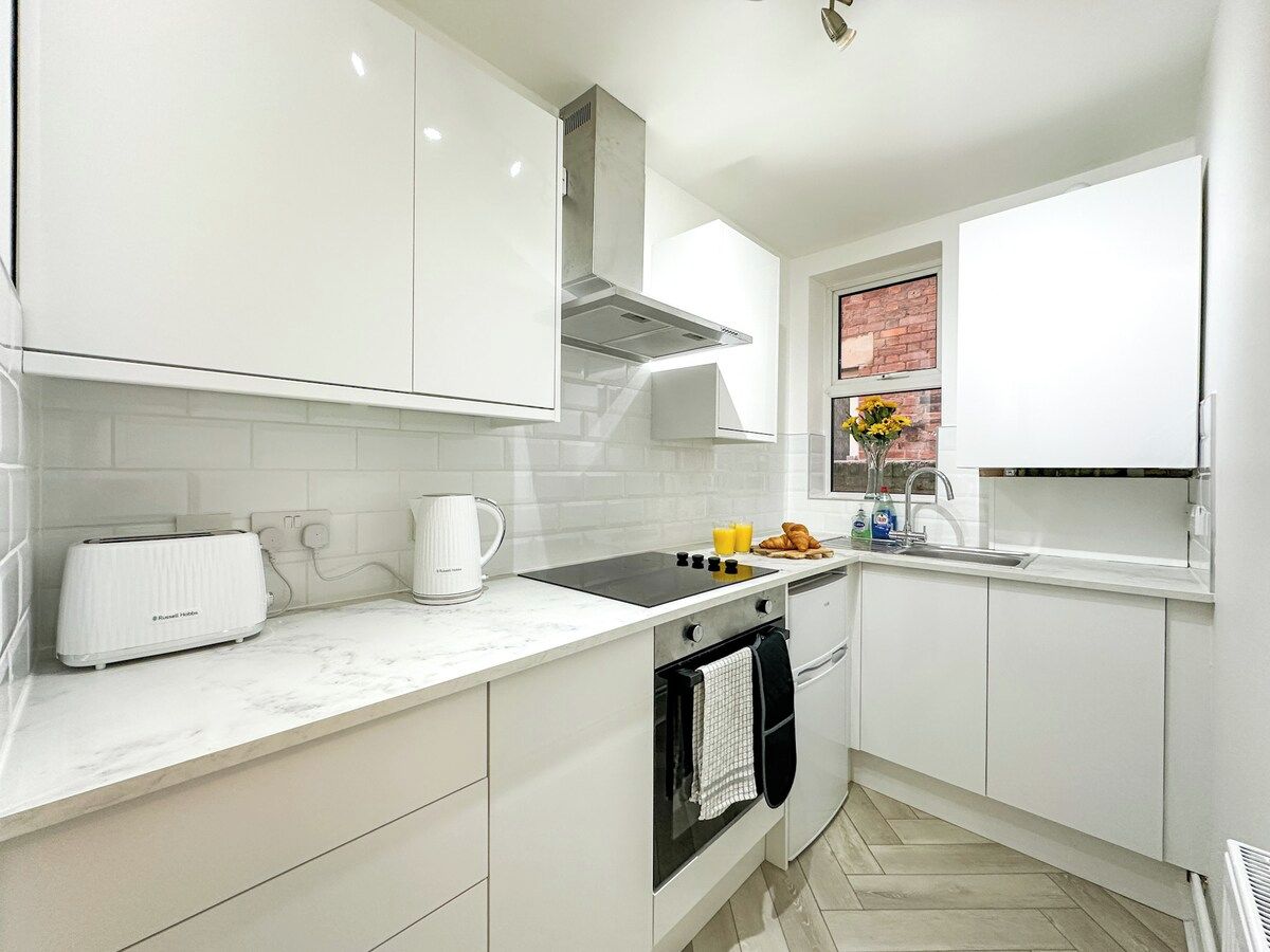 A modern kitchen with white cabinetry, a built-in oven, a stovetop, and a window with a view.