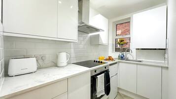 A modern kitchen with white cabinetry, a built-in oven, a stovetop, and a window with a view.