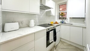 Una cocina moderna con armarios blancos, horno empotrado, estufa y ventana con vista a un muro de ladrillo.
