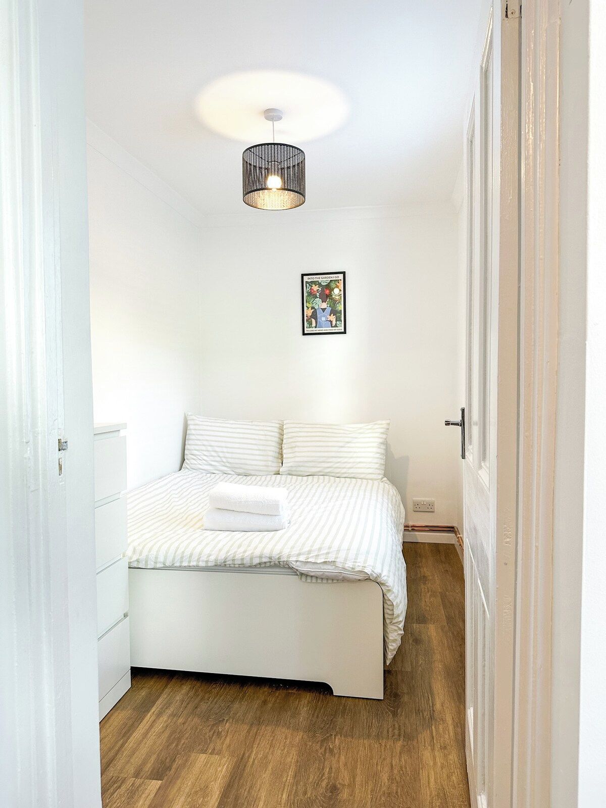 Un dormitorio con cama, lámpara colgante y un cuadro en la pared.