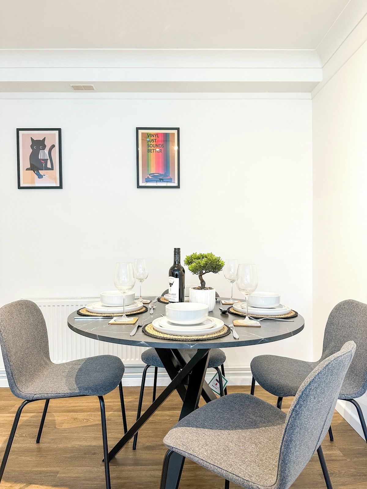 Comedor con una mesa redonda dispuesta para cuatro personas, rodeada de sillas tapizadas en gris.