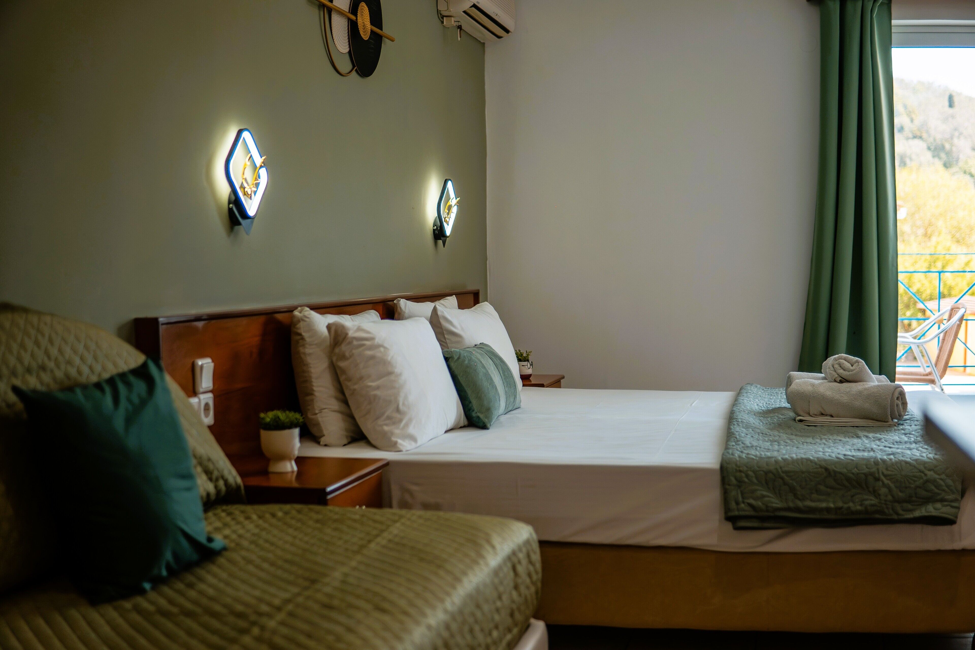 Habitación de hotel con dos camas, una mesita de noche con lámpara, un reloj de pared y una ventana con cortinas.