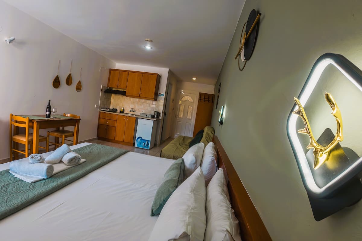 A hotel room with a bed, a desk with a chair, a kitchenette, and a bathroom.