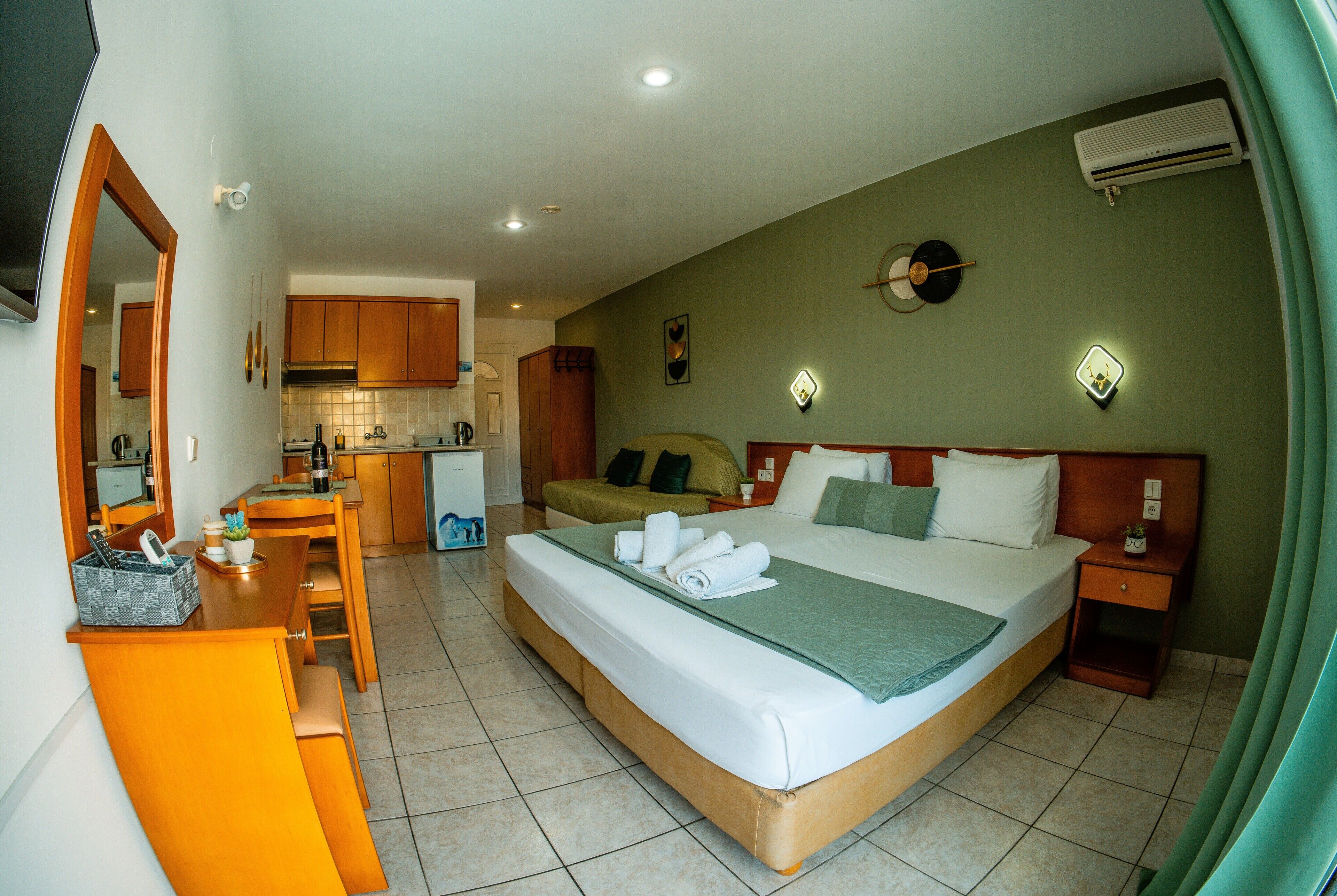 A hotel room with a bed, a desk, a kitchenette, and a bathroom.