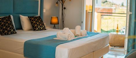 A neatly made bed with a blue blanket, white pillows, and towels, a floor lamp, and a view of the outside.